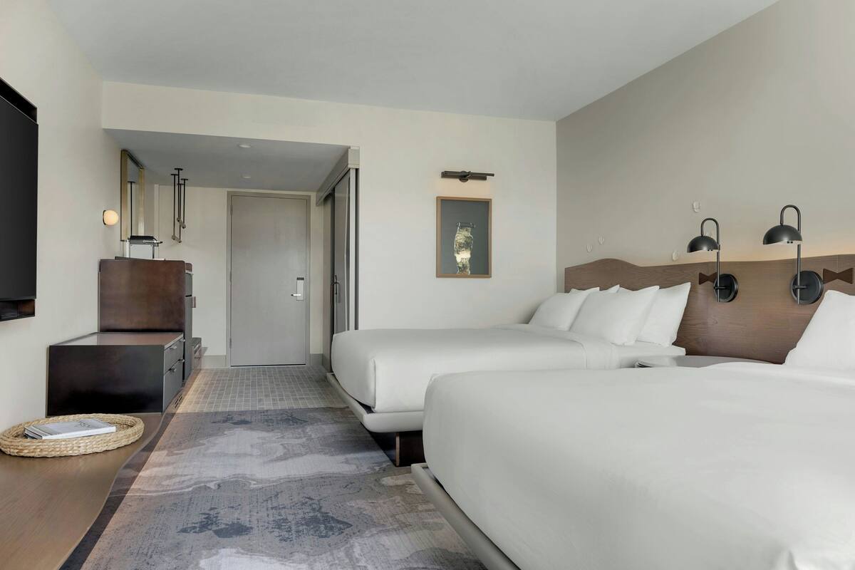 Habitación de hotel con dos camas, un escritorio, un espejo, una puerta y una lámpara fijada a la pared.