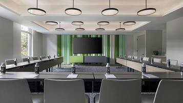 Un salón de conferencias con una larga mesa, sillas, una pantalla grande y una pared verde de acento.