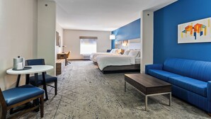 A hotel room with a bed, a blue sofa, a coffee table, a dining table with chairs, and a painting on the wall. - Holiday Inn Express and Suites Wytheville by IHG (Wytheville)