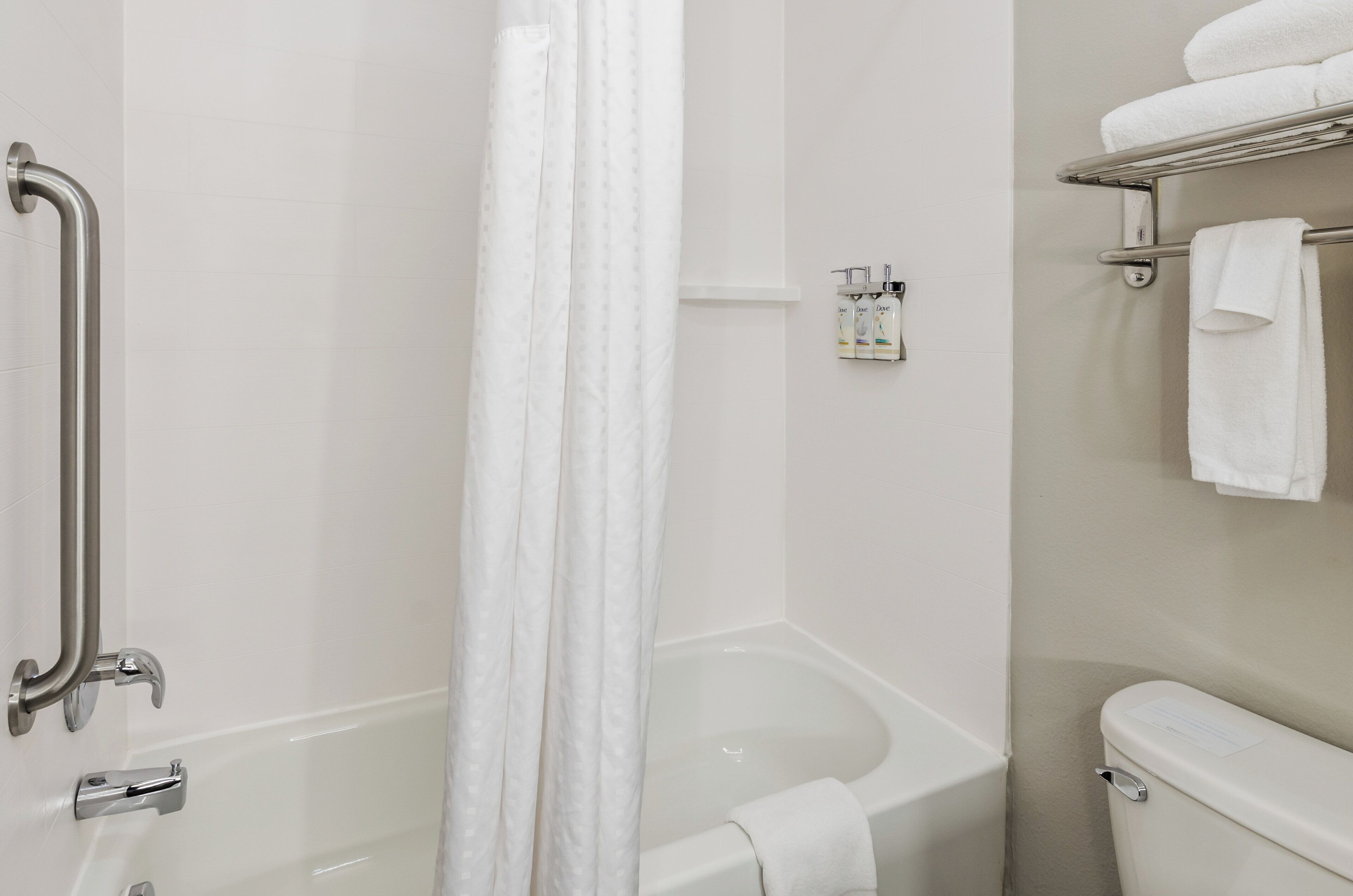 A bathroom with a bathtub, a shower area, a toilet, and a handrail.