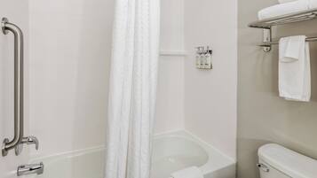 A bathroom with a bathtub, a shower area, a toilet, and a handrail.