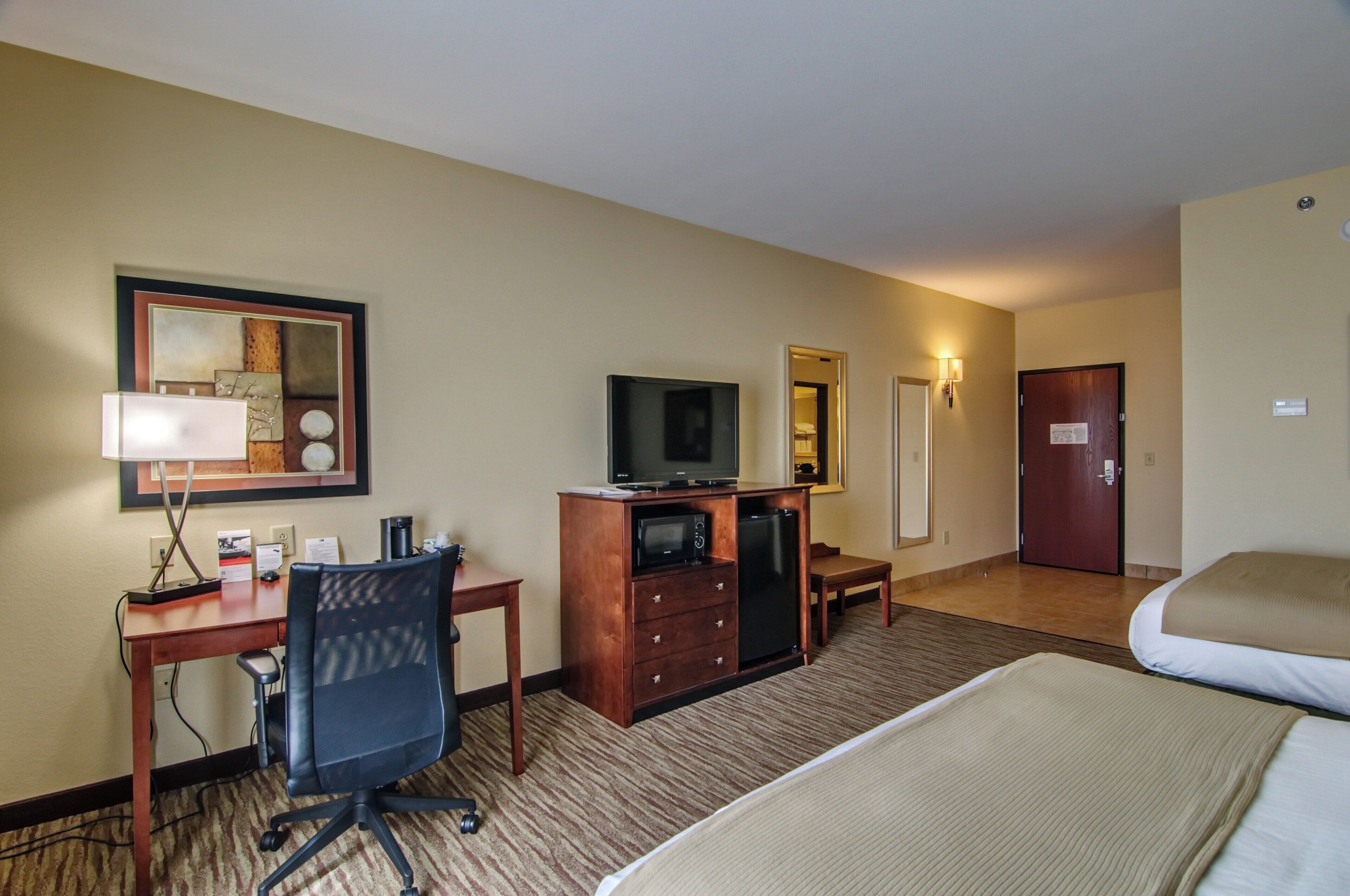 A hotel room with a bed, a desk with a chair, a television, a dresser, and a mirror.