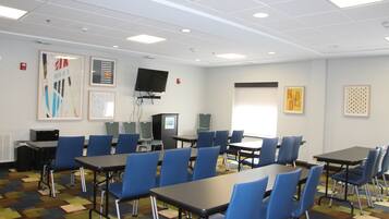 A conference room with multiple tables and chairs, a projector, and a television on the wall.