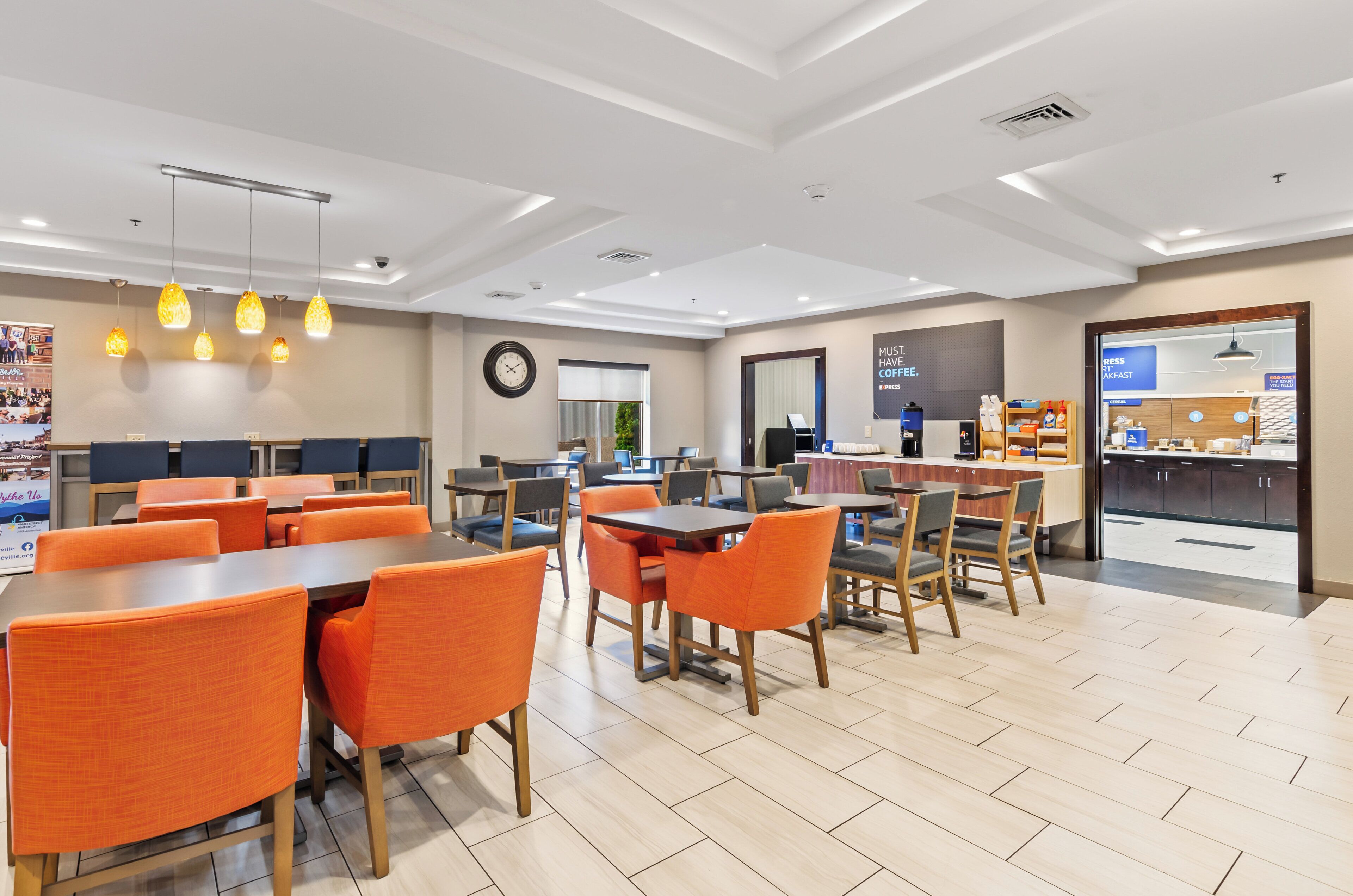 A modern dining area with orange chairs and tables, a coffee station, and a view of the outdoors.