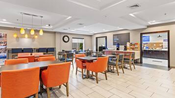 A modern dining area with orange chairs and tables, a coffee station, and a view of the outdoors.