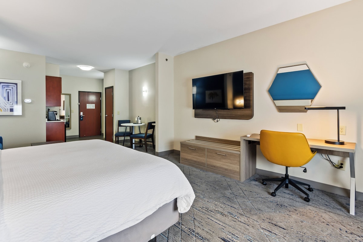 Quarto de hotel com uma cama grande, uma escrivaninha com cadeira, uma televisão e um candeeiro fixado na parede.