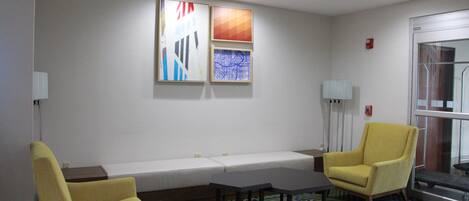 A conference room with a white table, two yellow chairs, a patterned rug, and abstract wall art.