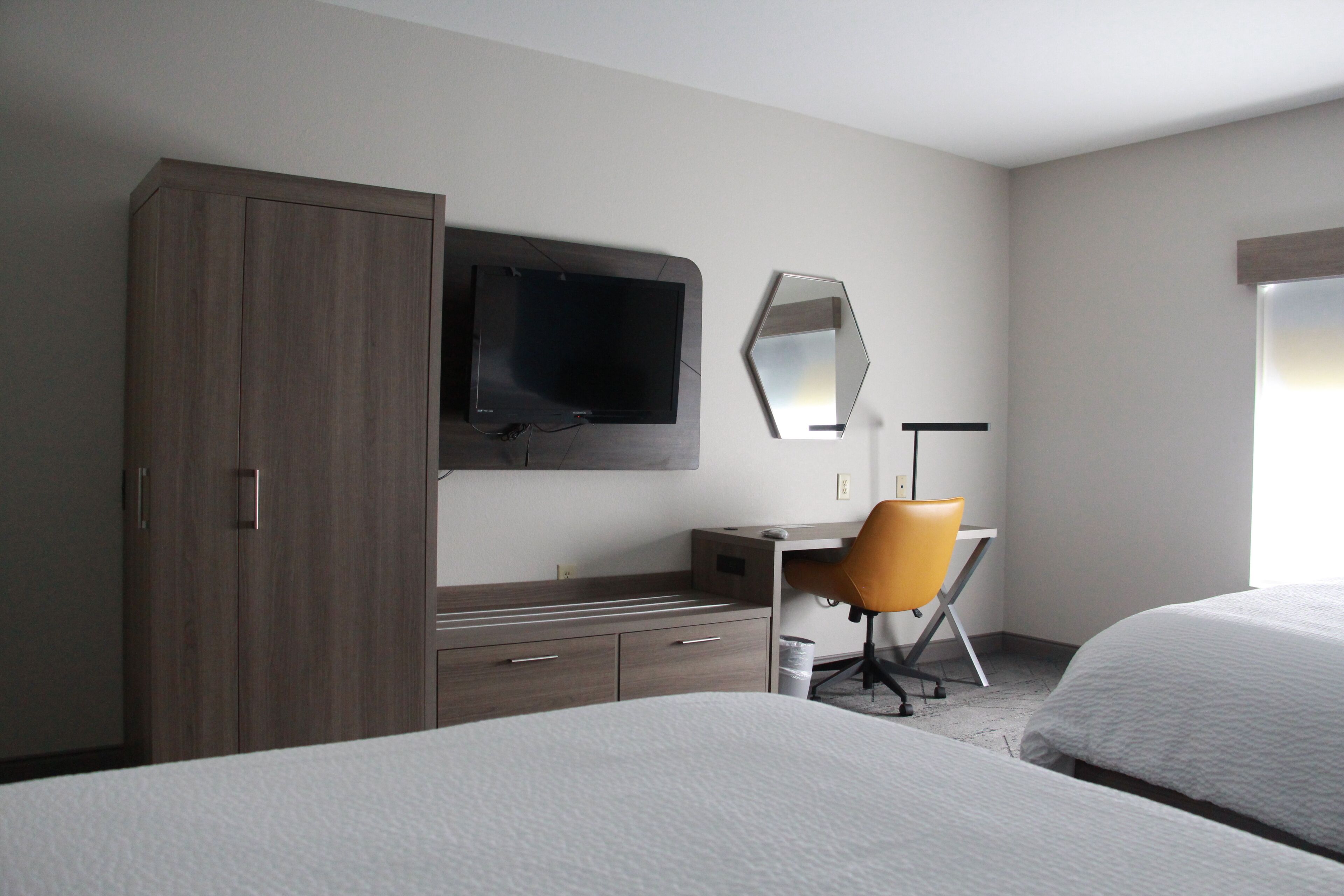Habitación de hotel con cama, escritorio con silla, televisor, armario y ventana grande.