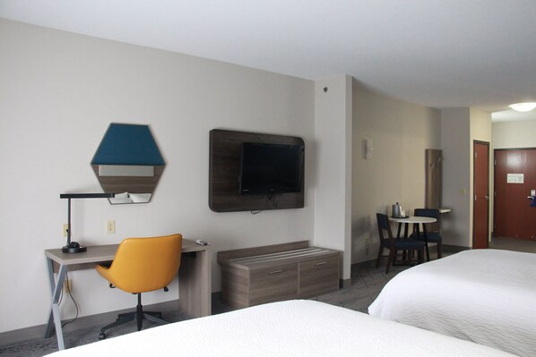Une chambre d’hôtel avec deux lits, un bureau avec une chaise, une télévision et une petite table avec des chaises.