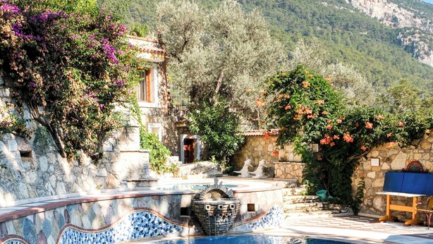 A swimming pool with a stone wall and a mountain backdrop. - Villa Symbola (Fethiye)