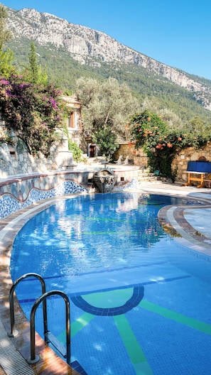 A swimming pool with a stone wall and a mountain backdrop. - Villa Symbola (Fethiye)