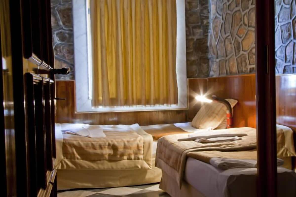 A room with two beds, a stone wall, a window with curtains, and a wooden door.