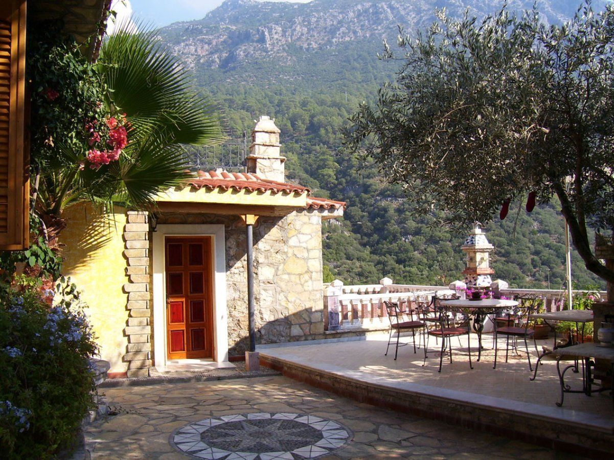 Un edificio de piedra con una puerta roja, un patio con suelo de baldosas y vista a la montaña.