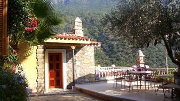 Un edificio de piedra con una puerta roja, un patio con suelo de baldosas y vista a la montaña.