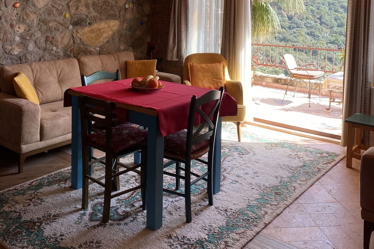 A dining area with a table set for two, a stone wall, and a view of a balcony with outdoor furniture.