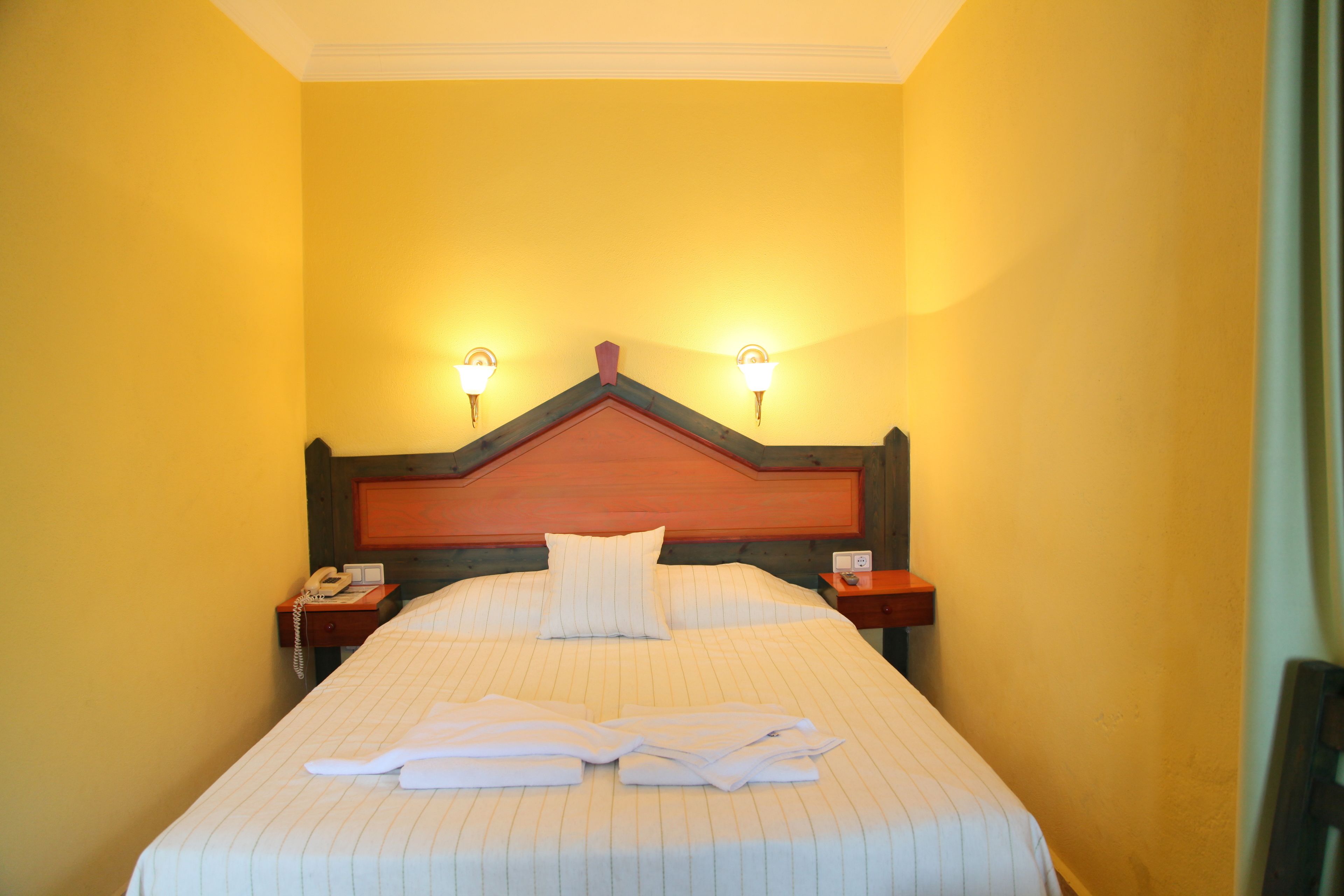 Habitación de hotel con una cama grande, dos lámparas de noche, un cabecero de madera y un teléfono en la mesita.