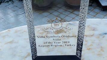 A clear award plaque on a marble table with a view of a balcony and greenery.
