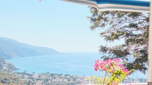 A terrace with a view of the sea, a table, chairs, and a blue-striped umbrella. - Villa Symbola (Fethiye)