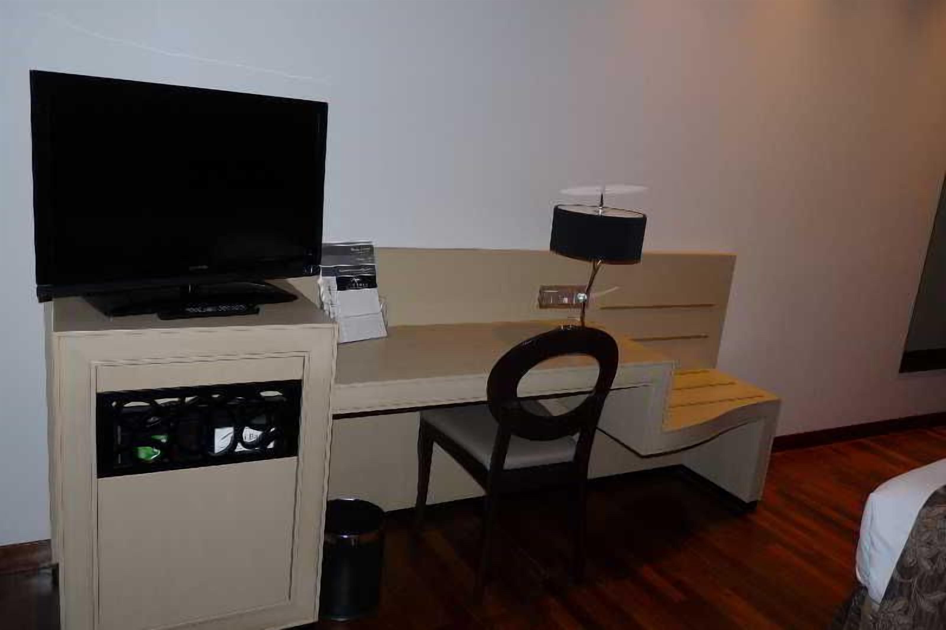 Una camera d'albergo piccola con un letto, una scrivania con un computer, una televisione e una sedia.