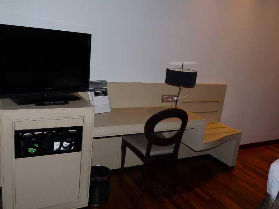 Una camera d'albergo piccola con un letto, una scrivania con un computer, una televisione e una sedia.