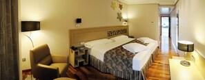 A hotel room with a bed, a chair, a desk, and a lamp. - Cumbria Spa&hotel (Ciudad Real)