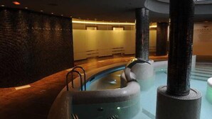A modern indoor pool area with a curved design, a glass wall, and a wooden floor. - Cumbria Spa&hotel (Ciudad Real)