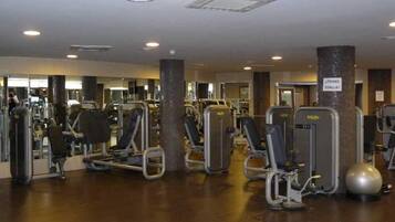 Un gimnasio con diversas máquinas de ejercicio, un espejo grande y un letrero que dice 'Tienes toalla?'.