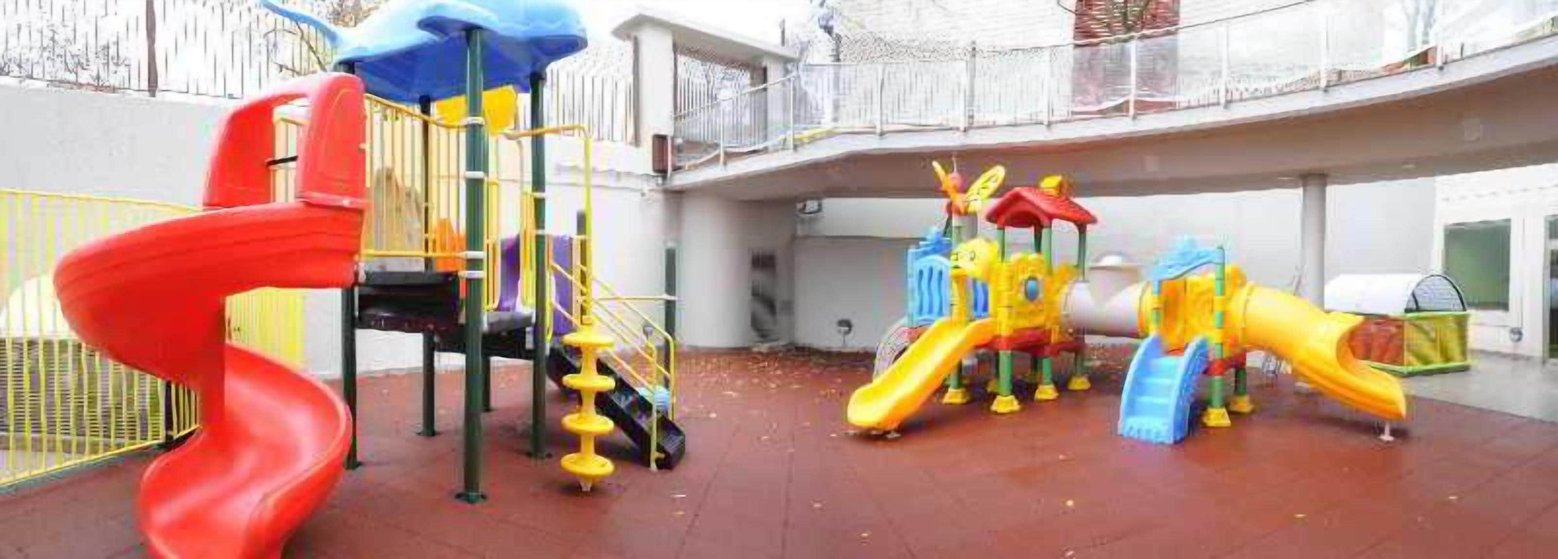 Un espace de jeux pour enfants avec un toboggan rouge en forme de spirale, une structure d’escalade jaune et bleue, et un toboggan jaune.