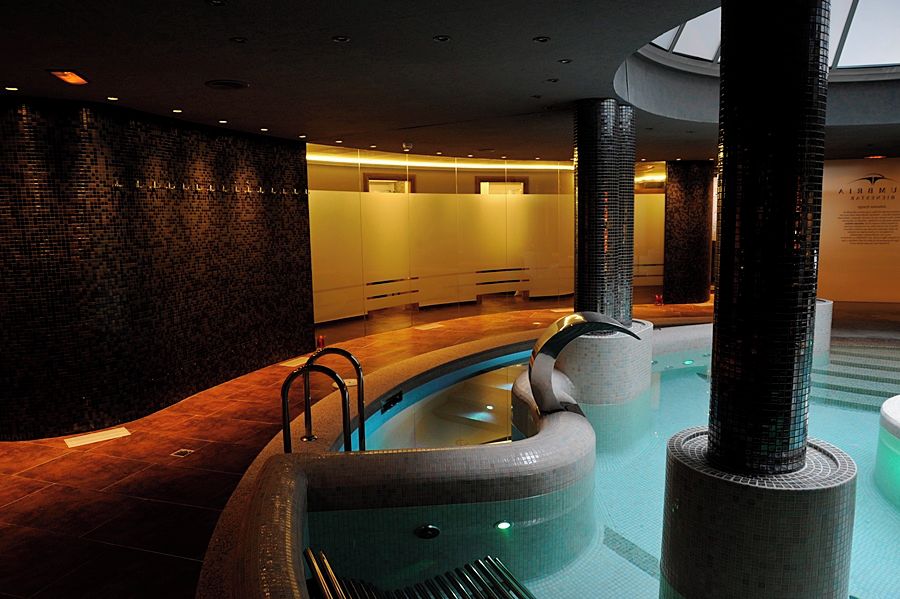 Un área interior de piscina moderna con diseño curvo, una zona de estar con mostrador de recepción y una pared de ladrillo.