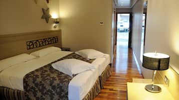A hotel room with a large bed, a bedside table with a lamp, and a hallway leading to a door.