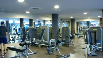 A gym with various exercise machines, mirrors, and a person using a machine.