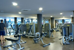 A gym with various exercise machines, mirrors, and a person using a machine. - Cumbria Spa&hotel (Ciudad Real)