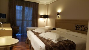 A hotel room with two beds, a desk, a chair, and a large window with curtains. - Cumbria Spa&hotel (Ciudad Real)