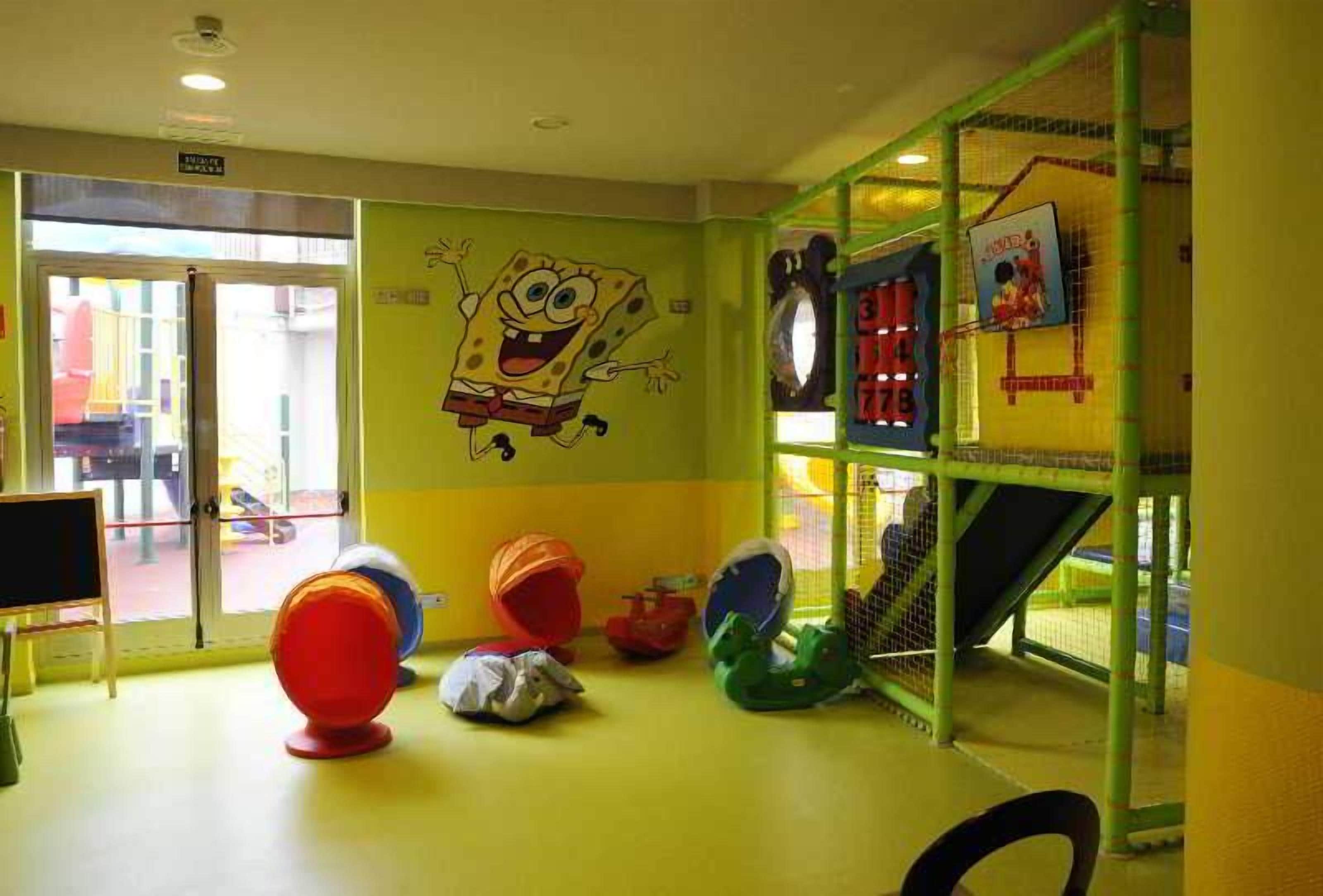Un espace de jeux pour enfants avec un personnage de dessin animé peint sur le mur, un toboggan et des jeux colorés.