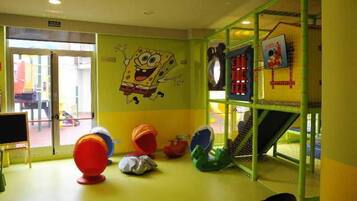 Un espace de jeux pour enfants avec un personnage de dessin animé peint sur le mur, un toboggan et des jeux colorés.