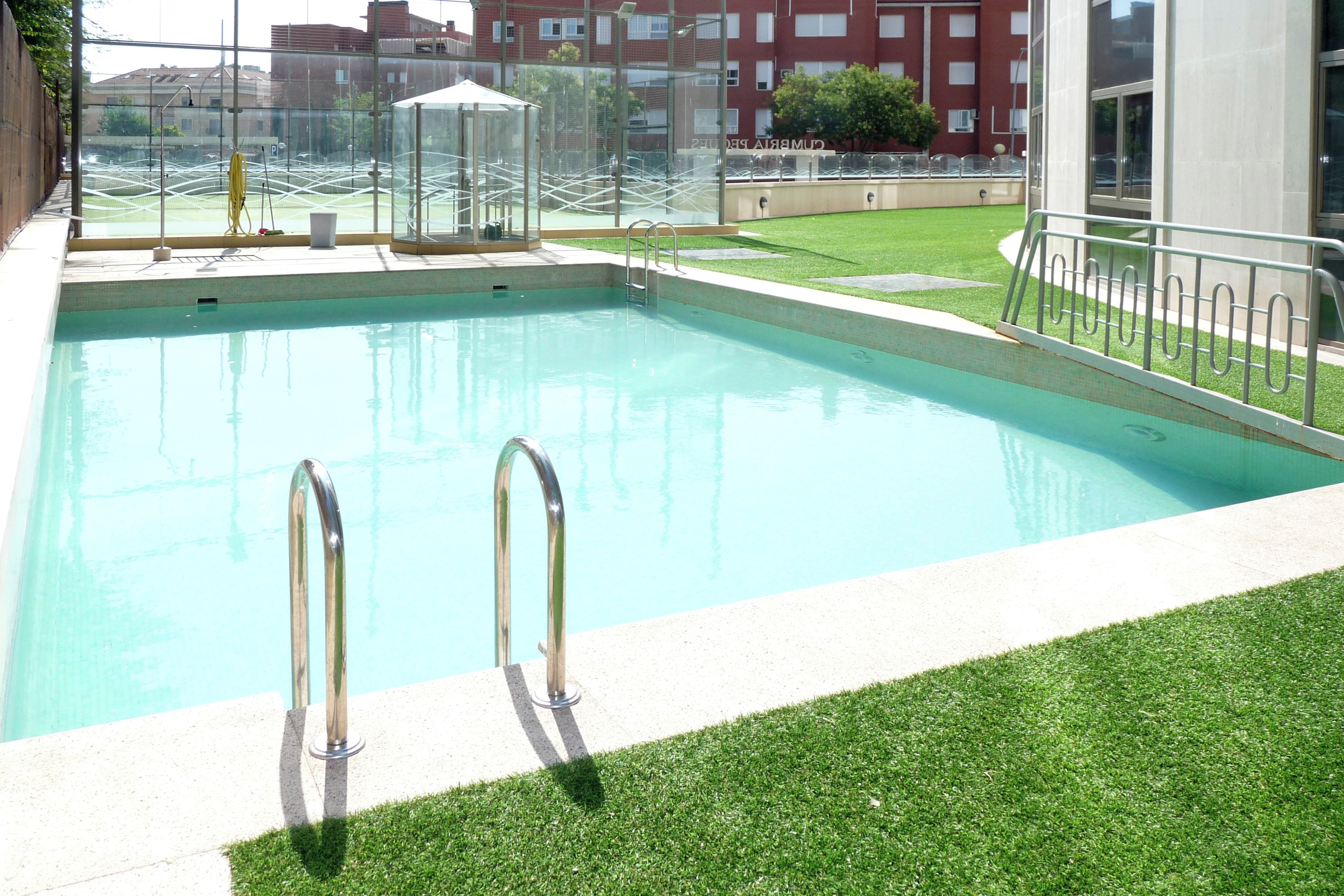 A swimming pool with two metal ladders, surrounded by a grassy area and a glass enclosure.