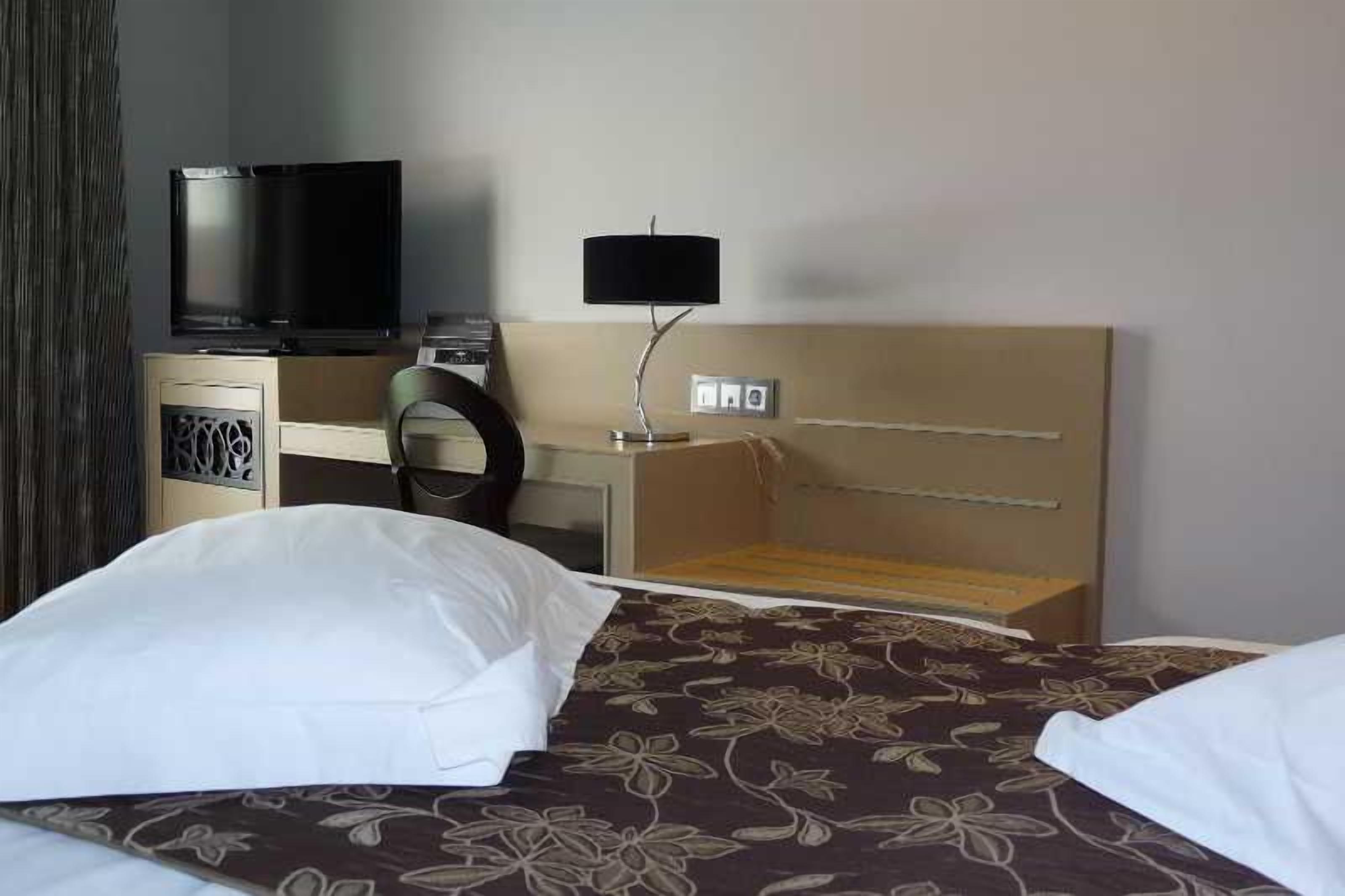 Ett hotellrum med en säng, en tv, ett skrivbord med en lampa och en garderob.
