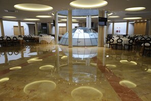 A spacious hall with a central glass dome structure, multiple tables with chairs, and a polished marble floor. - Cumbria Spa&hotel (Ciudad Real)