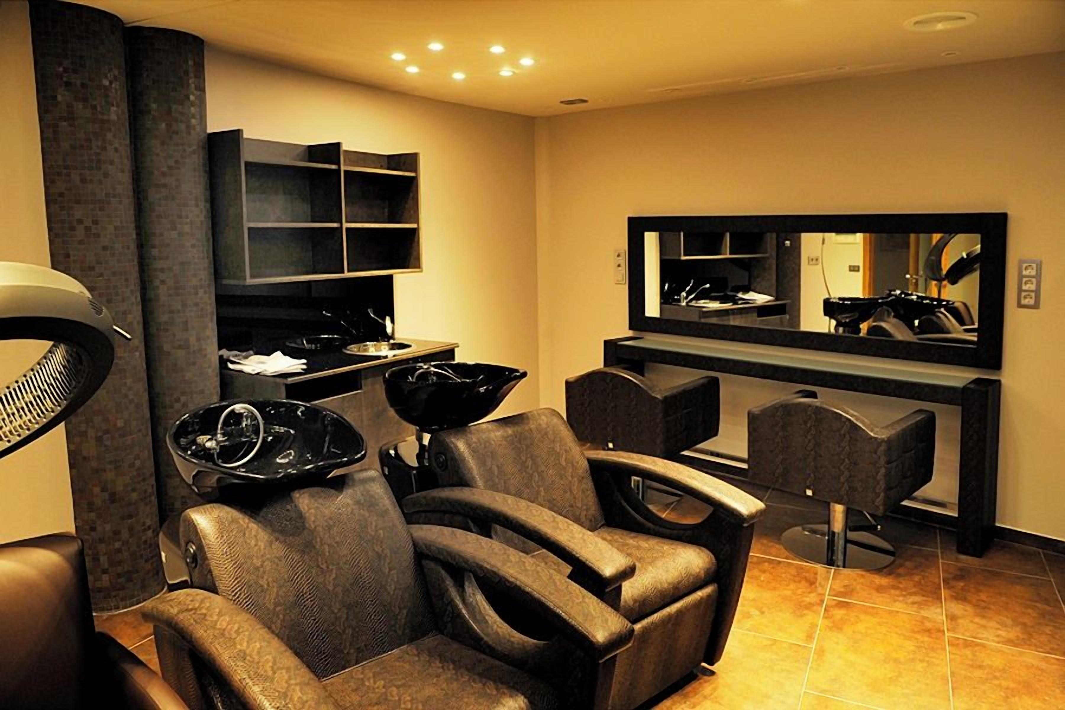 Un salon de coiffure moderne, avec des fauteuils en cuir, un grand miroir et une console noire.