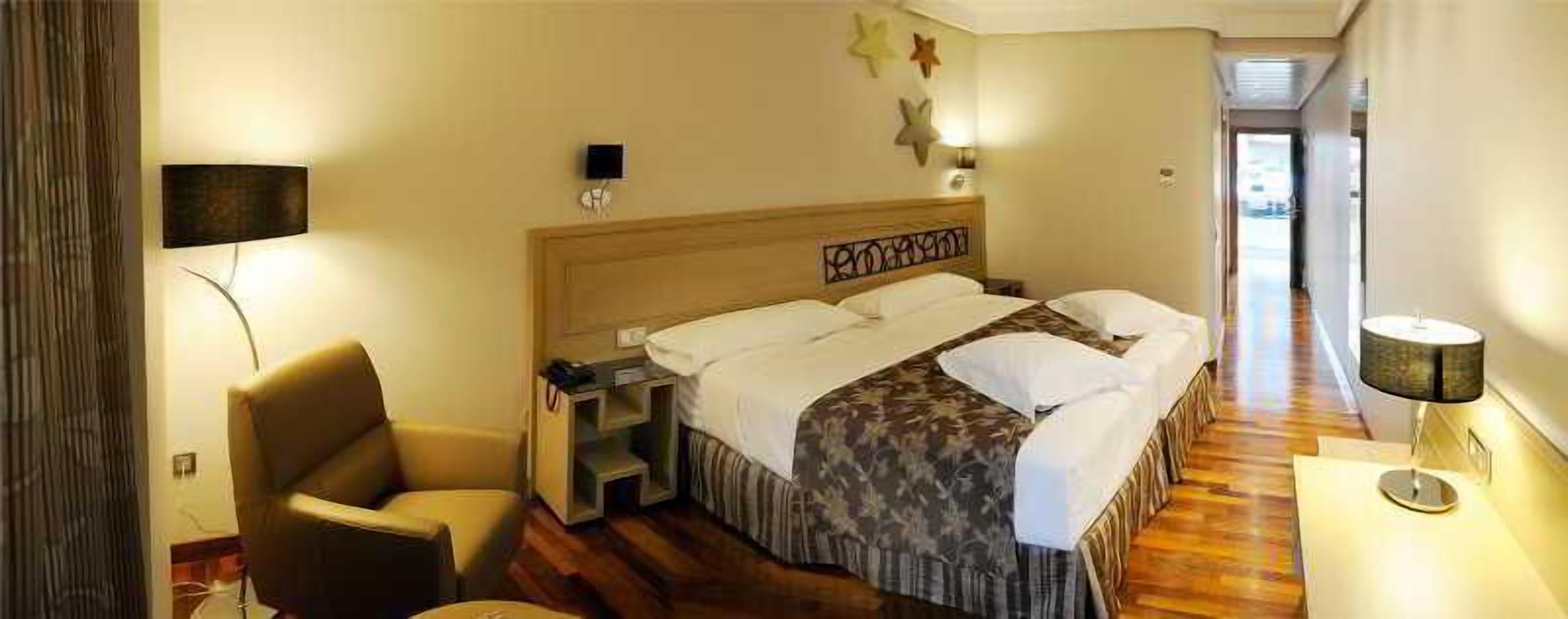 Ett hotellrum med en säng, en stol, ett skrivbord och en lampa.