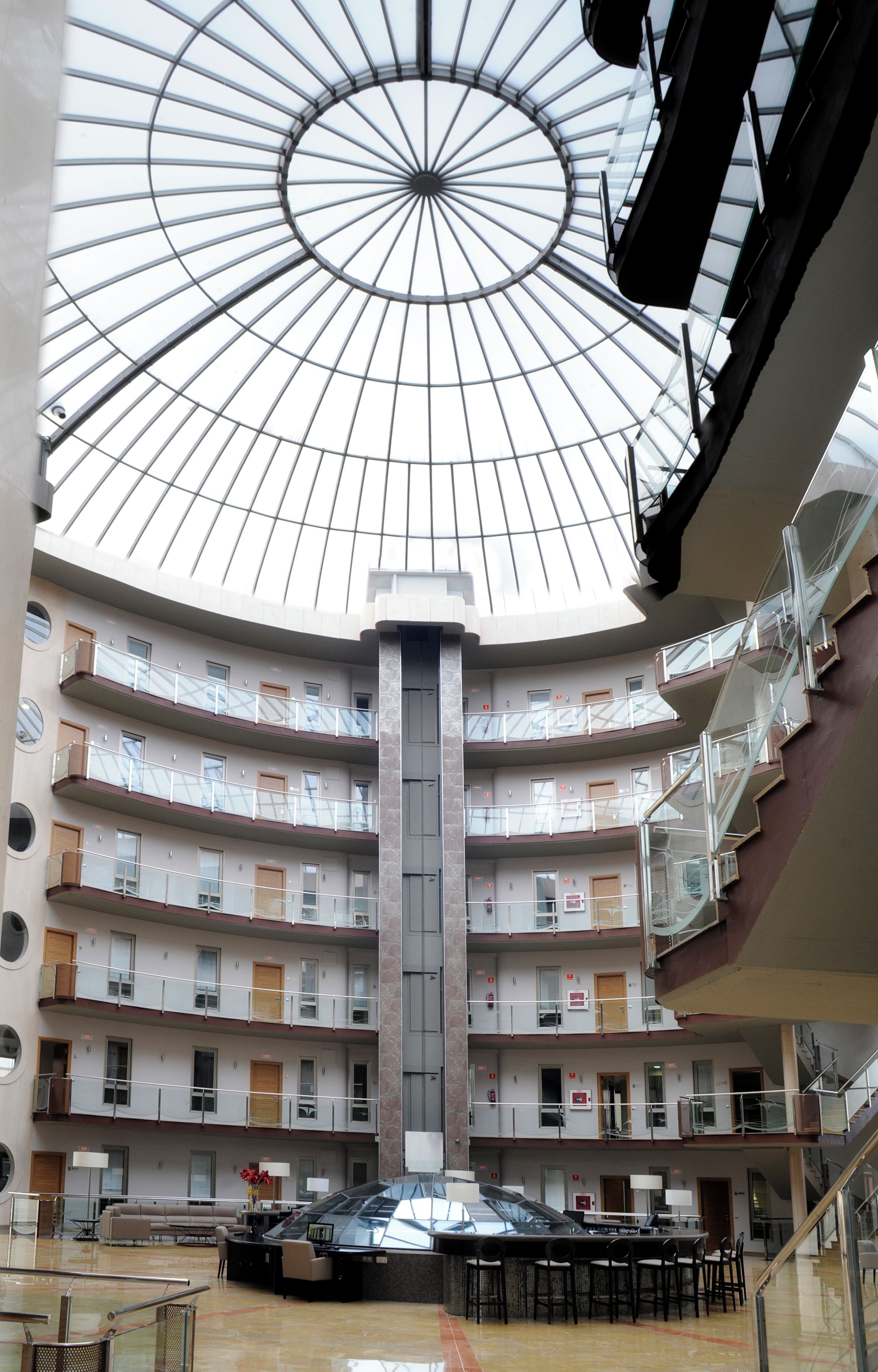 Un atrio de varios niveles con cúpula de cristal, múltiples balcones y una escalera central.