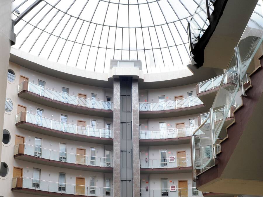 Un atrio de varios niveles con cúpula de cristal, múltiples balcones y una escalera central.
