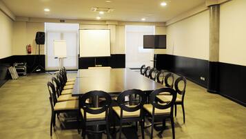 Un salón de conferencias con una larga mesa, sillas, un proyector y una pantalla.