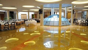 A spacious banquet hall with round tables and chairs, a central glass dome structure, and a polished marble floor. - Cumbria Spa&hotel (Ciudad Real)