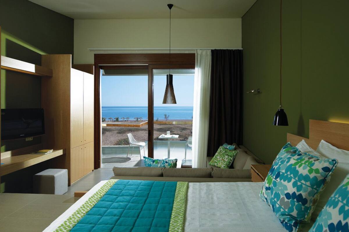 A hotel room with a bed, a TV, a sofa, and a view of the sea.