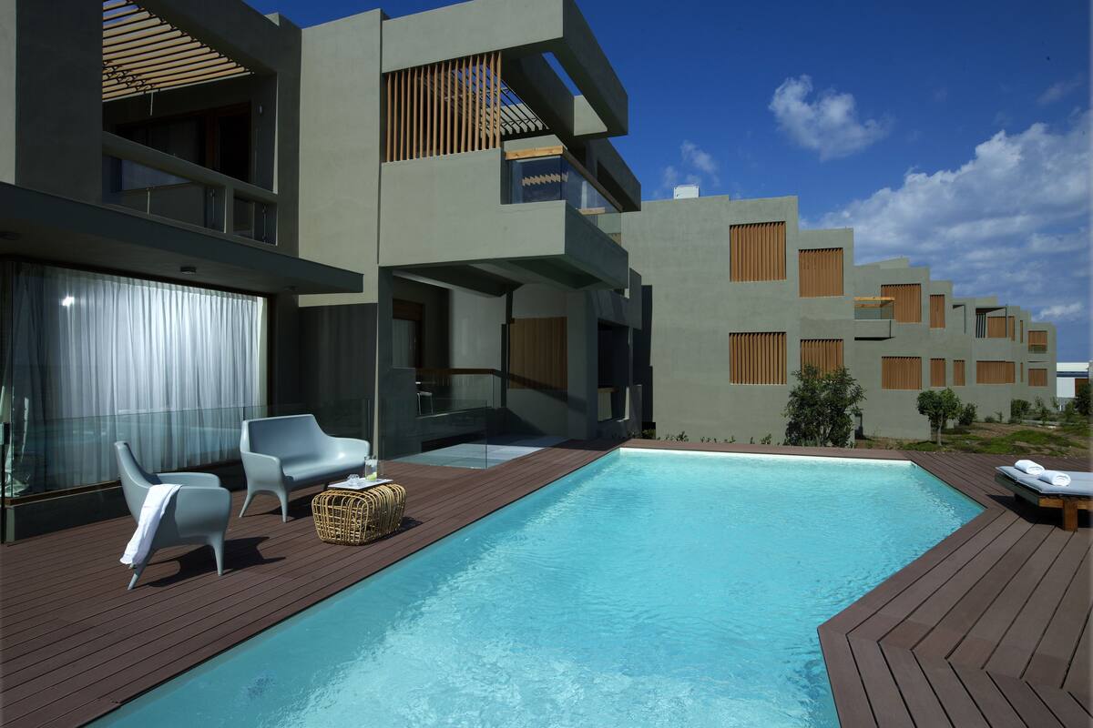 A modern hotel with a swimming pool, outdoor seating, and a clear blue sky.