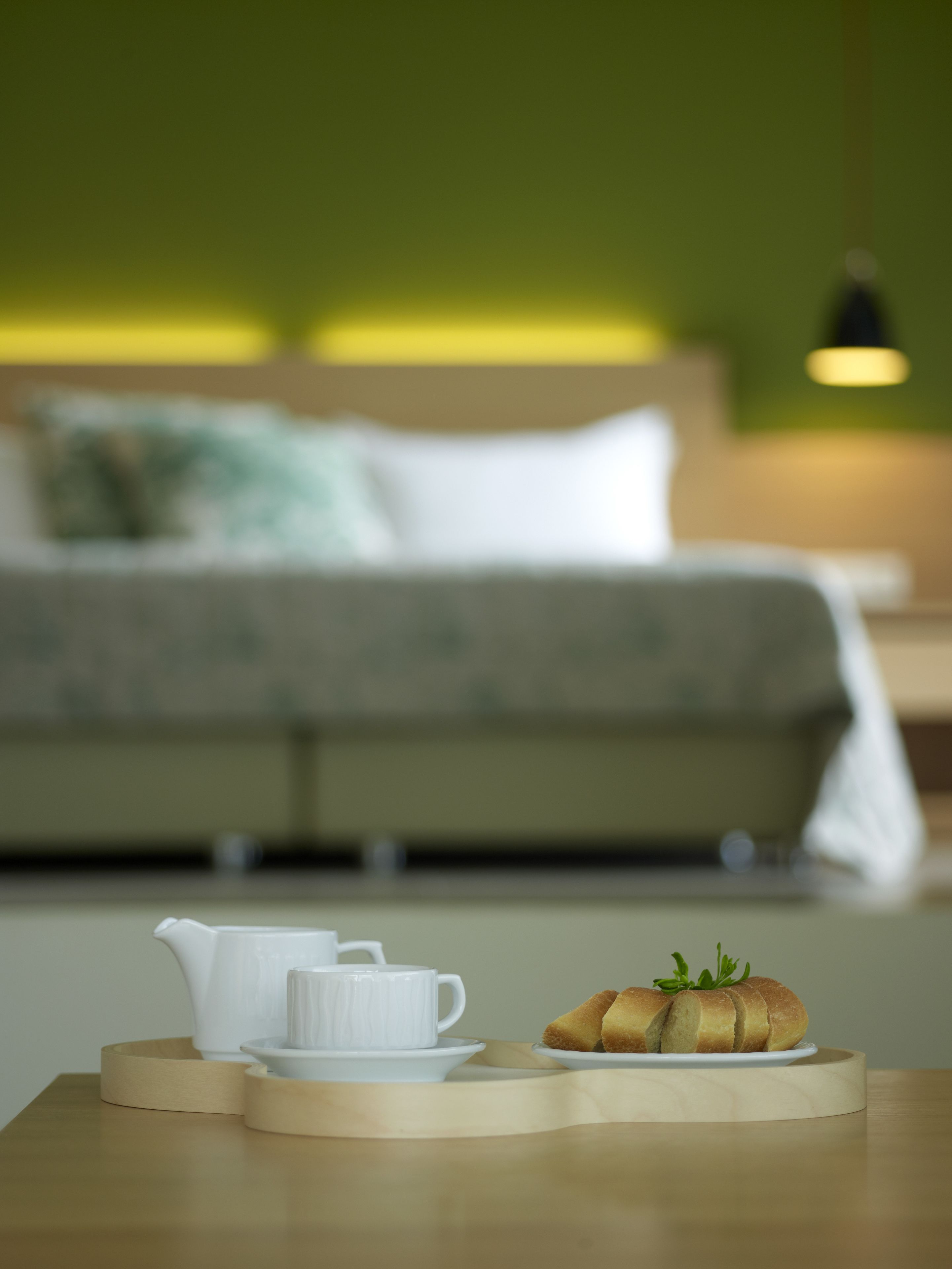 Frühstücksausrüstung mit Teekanne, Tasse und Croissant auf einem Holztisch in einem Hotelzimmer, im Hintergrund ein Bett.