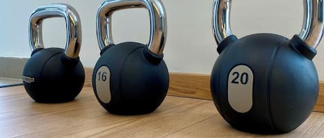 Three kettlebells with weights of 16, 20, and an unspecified weight on a wooden floor.