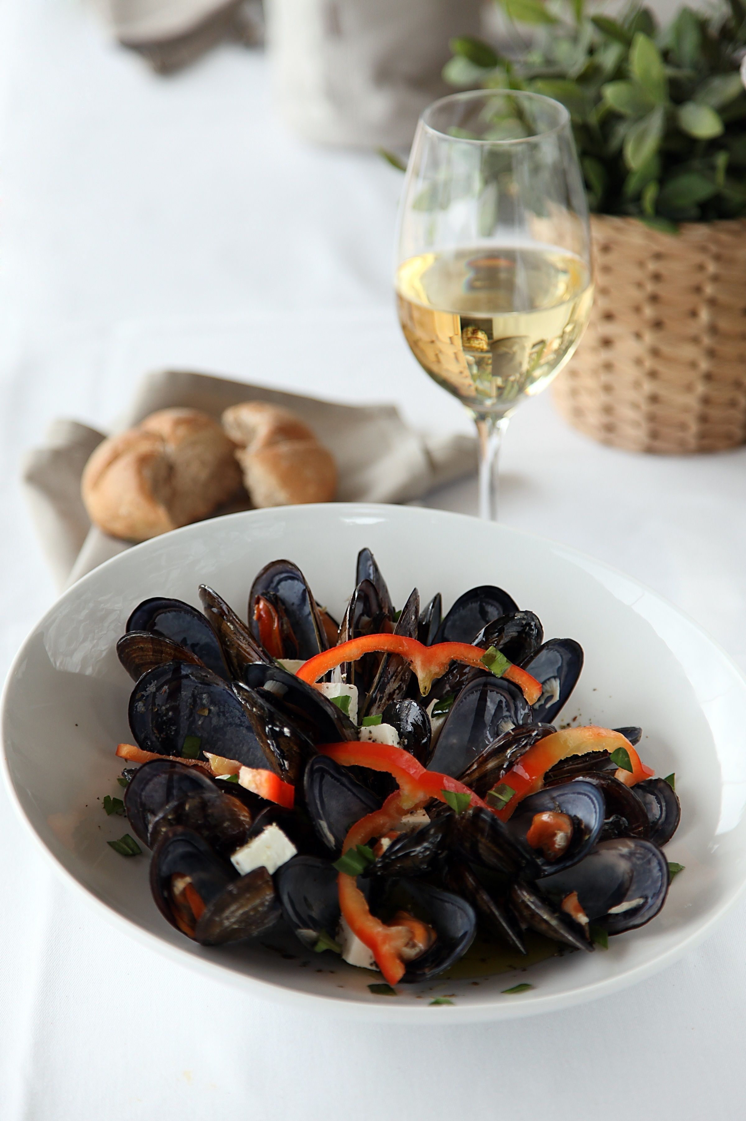 Una ciotola di cozze con verdure e un bicchiere di vino bianco su un tavolo.