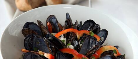 Una ciotola di cozze con verdure e un bicchiere di vino bianco su un tavolo.